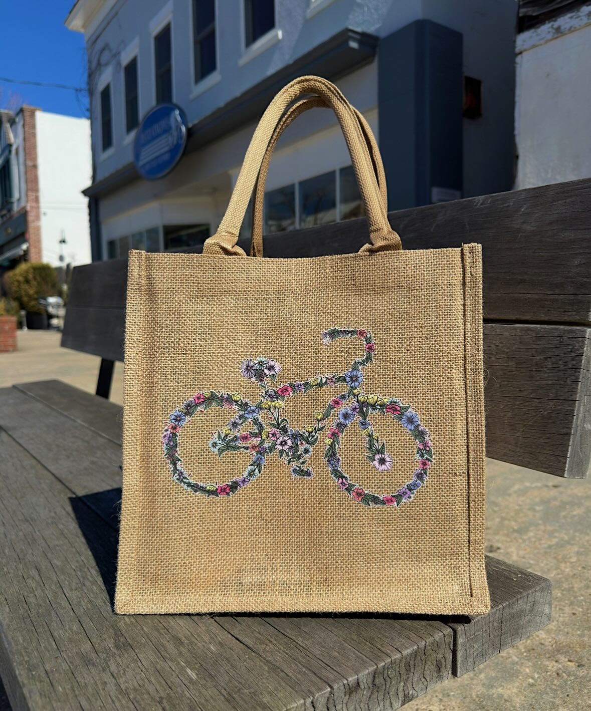Real floral bicycle burlap tote on a wooden bench, showing the fabric texture and printed artwork