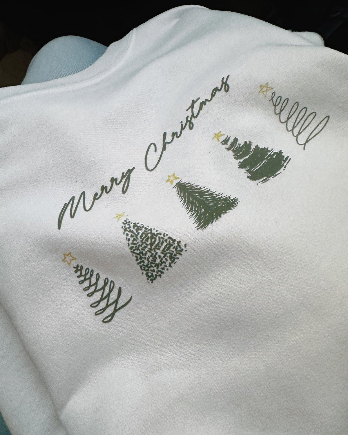 Real Merry Christmas crewneck close-up showing the five green trees and gold stars